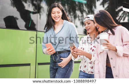 Happy asian friends using smartphones at bus station - Young students people having fun with technology trends after school - Friendship and transports app concept - Focus on center girl face Royalty-Free Stock Photo #1388898497