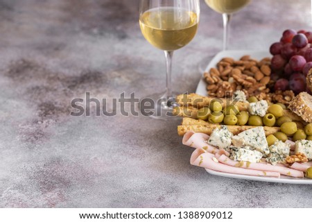 Two glasses of white wine and plate with different snacks. Blue cheese, olives, baguette slices, grissini, ham, grapes and nuts. Wine snacks set background.Copy space