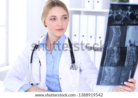 Doctor woman examining x-ray picture near window in hospital. Surgeon or orthopedist at work. Medicine and healthcare concept. Blue colored blouse of a therapist looks good