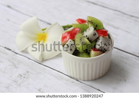 Fruit salad in white porcelain bowl, Kiwi fruits, apples, dragon fruits on wooden background, Diet food, Fresh vitamins