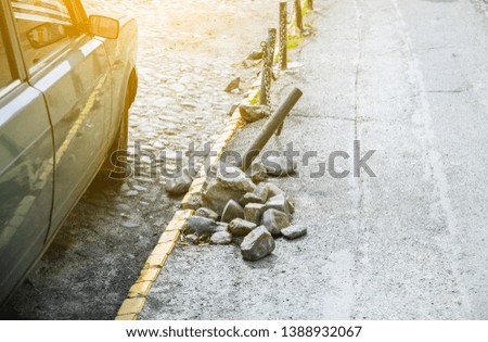 Broken road in the city. Fence on the sidewalk. Stones pavement.