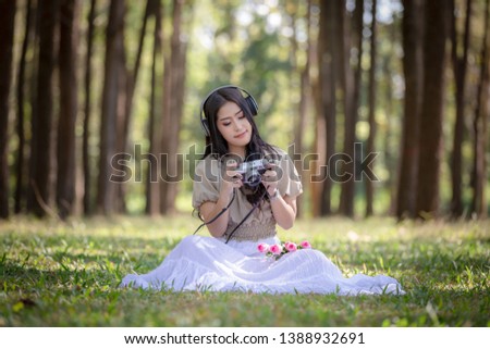 woman asian girl sitting relax listening to music on headphones Bluetooth and camera shooting on holding hand in the park  pine forest summer holiday travel concept