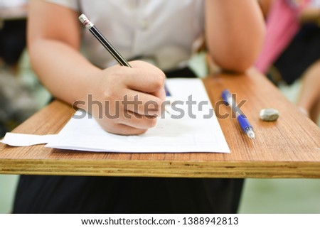 Girl Student holding a pencil writing or taking final test in an examination room of the collage or university exam or training center - education concept pic of classroom assignment or learning