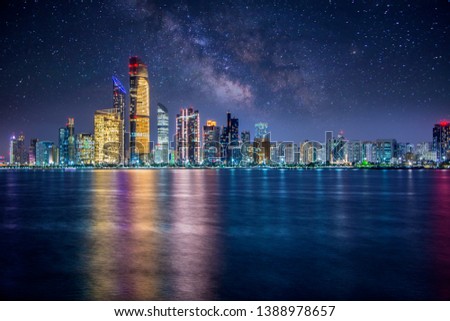 Abu Dhabi city at night with lights reflections and a milky-way sky.