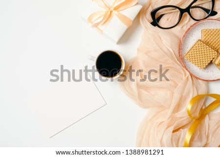 Female workspace with blank paper card, scarf, golden accessories, glasses, ribbon, gift box, coffee cup on white background. Flat lay beauty blogger home office desk. Top view feminine background