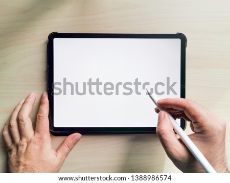 flat lay top above photo of 11 inches new pro tablet empty screen with pen and male hands holding it on wooden desk. ready to use for mockups