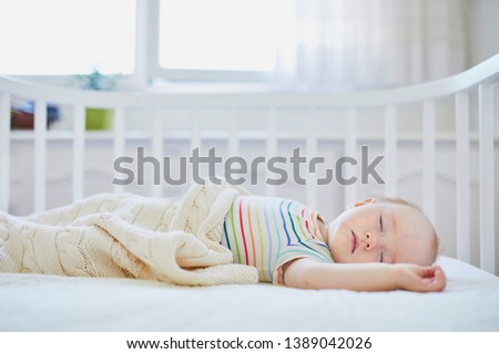 Adorable baby girl sleeping in co-sleeper crib attached to parents' bed. Little child having a day nap in cot. Sleep training concept. Infant kid in sunny nursery Royalty-Free Stock Photo #1389042026