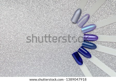 Nail art color palette. Set of blue, violet and lilac artificial nails and manicure samples, on a festive silver glitter background. Top view, flat lay, space for text. Nail studio advertisement.