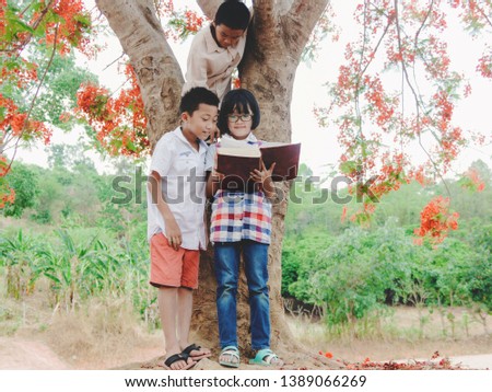Asian children reading a book under big flower tree