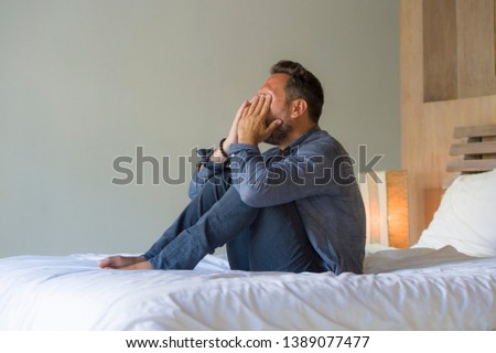 lifestyle home portrait of young attractive overwhelmed and depressed man sitting on bed worried and frustrated suffering depression crisis covering face with hands feeling desperate and helpless Royalty-Free Stock Photo #1389077477