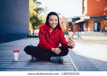 Millennial asian woman posing for selfie photo while taking rest on urban setting, happy chinese hipster girl enjoying time for using modern mobile technology and creating content of pictures