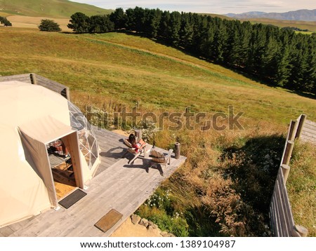 Aerial view of woman at white geodome tents. Glamping view from above, shot on DRONE. Green, nature background. Cozy camping vacation lifestyle concept. Outdoors, scenic background. New Zealand.