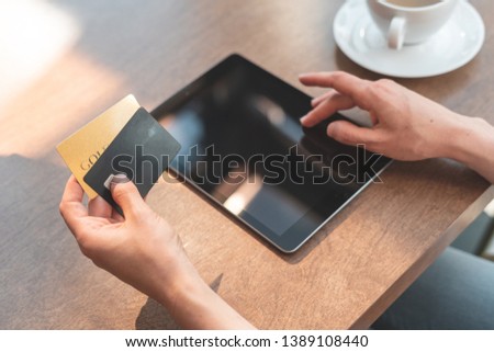 Close up cropped photo of young successful woman spending weekend day in cozy cafe with comfort and modern interior with bright light room. Female using tablet with credit card for online shopping
