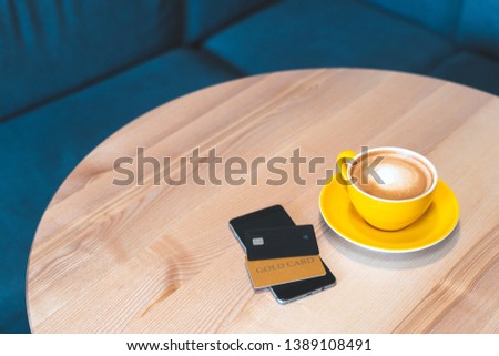 High angle above top view or overhead, flat lay photo of cafe with modern interior, soft and natural daylight. Digital gadget or smartphone with two plastic bank card lying on wooden table
