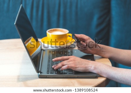 Cropped photo of young or adult woman spending weekend day in cozy cafe with bright light and modern interior. Female using personal computer and making online shopping with bank card