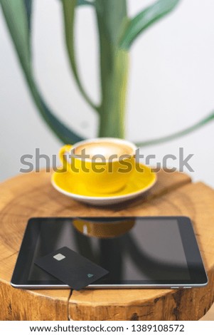 High angle above top view or overhead, flat lay photo. Modern digital tablet with plastic card and cup of coffee lying on wooden table in cafe with modern interior with soft and natural daylight