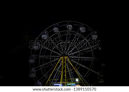 The Ferris wheel bianglala/carousel at night. It is with low lighting. Side view. 