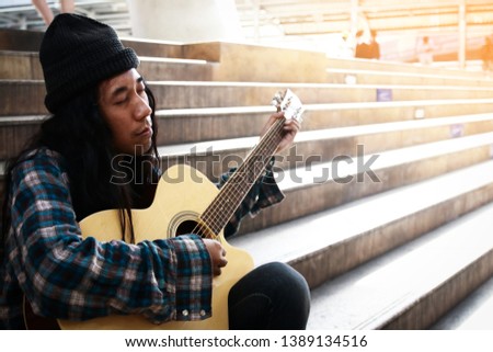 Homeless man holding a guitar, playing music, asking for money at the pedestrian staircase