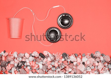 Coffee cap headphones plugged into coffee cup on coral background
