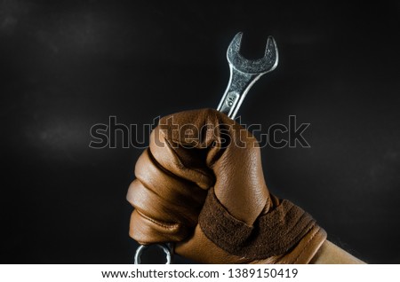 a wrench was holding by leather glove man hand in dark light