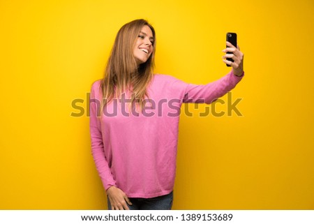Woman with pink sweater over yellow wall making a selfie