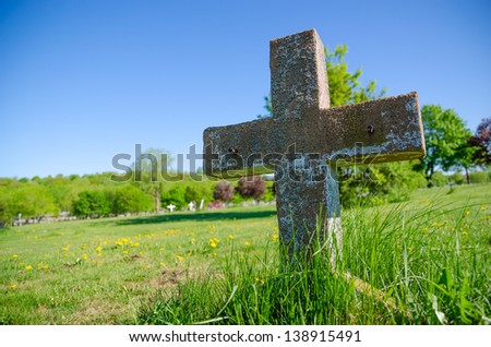 Old cross headstone in a cemetery, with blue sky and green grass