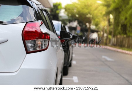 Closeup of rear or back side of white car with  other cars parking in parking area beside the street in bright sunny day. The mean of simply transportation in modern world.