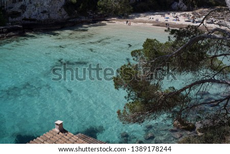 A laguna on the coast of Mallorca. Water of the Mediterranean Sea seen from above in a narrow bay forming a diagonal of the picture. Sandy beach and green vegeataion forming the frame. Sunlight lit.