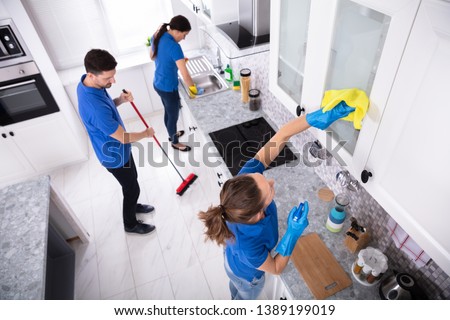 Group Of Young Janitors In Uniform Cleaning Kitchen At Home Royalty-Free Stock Photo #1389199019