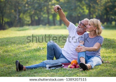 Happy senior couple relaxing in park using smartphone taking selfie photo  together .old people sitting in the summer park looking mobile phone and video call . Elderly resting .mature relationships 