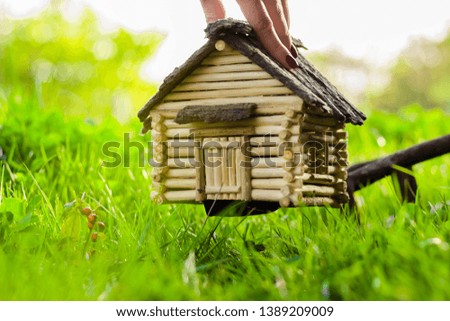 Eco-friendly wooden house on the grass. The girl raises the house with his hand and puts