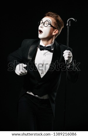 surprised mime man in tuxedo and glasses posing with walking stick on black background