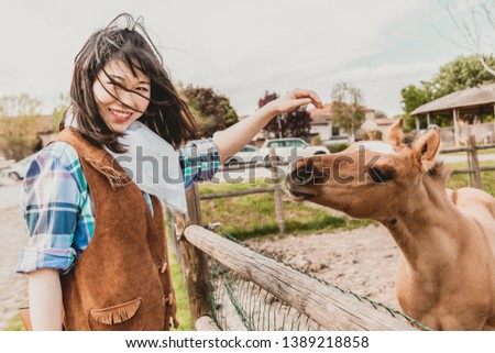 Portrait of a beautiful Chinese female cowgirl while stroking a foal in her fence