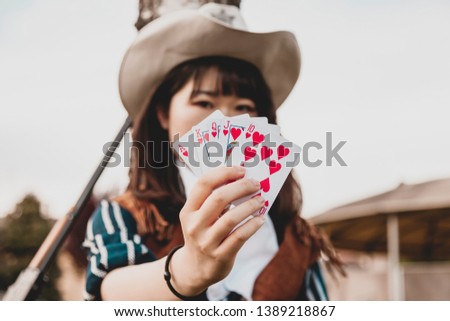 Portrait of a beautiful Chinese female cowgirl while playing with poker cards sitting outdoors