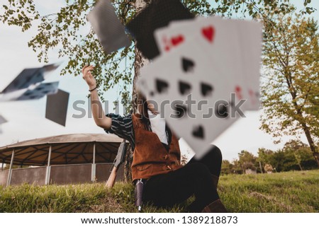Portrait of a beautiful Chinese female cowgirl while playing with poker cards sitting outdoors