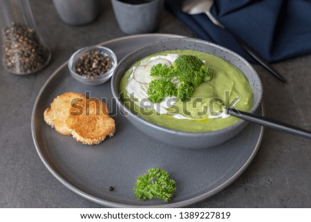 Side view diet cream soup with broccoli and sour cream with radish, spoon, pepper and napkin near on concrete gray background. Concept of diet summer food. Space for text