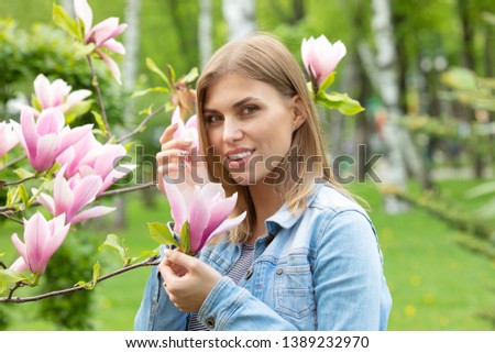 Beauty young woman enjoying nature in spring spring magnolia flowers. Beautiful blonde girl in Garden with blooming magnolia trees. Smiling girl with blossom flowers outdoors.