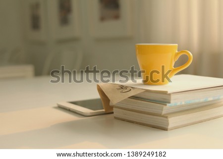  cup of coffee placed on a book stack with a tablet placed on a white table with natural light