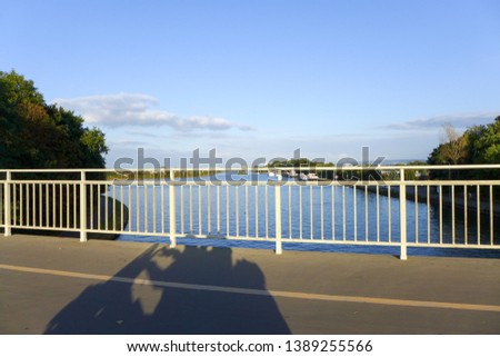 Shadow of a moving motorcycle with driver and passenger on a bridge overlooking a river