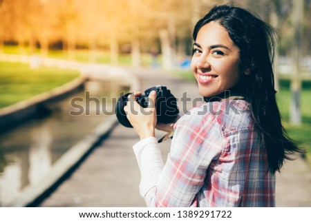 Happy excited tourist shooting landmarks. Rear view of beautiful girl in casual shirt holding photo camera, turning round and smiling. Tourism and walk concept