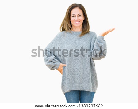 Beautiful middle age woman wearing winter sweater over isolated background smiling cheerful presenting and pointing with palm of hand looking at the camera.