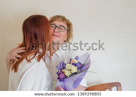 Daughter giving flowers to adult mother. Daughter gives flowers to her mother and hugs her. Spending time together, celebrating at home on weekends. Mothers Day