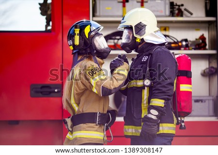 Image of firefighters women and men in helmet and mask looking at each other and doing handshake near fire truck