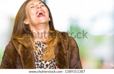 Beautiful middle age elegant woman wearing mink coat Smiling and laughing hard out loud because funny crazy joke. Happy expression.
