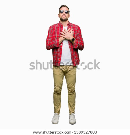 Handsome man wearing fashion sunglasses smiling with hands on chest with closed eyes and grateful gesture on face. Health concept.