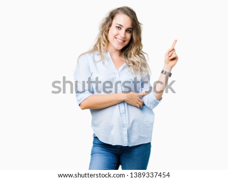 Beautiful young blonde business woman over isolated background with a big smile on face, pointing with hand and finger to the side looking at the camera.