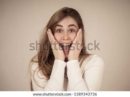 Beautiful young blonde teenager woman with happy face making surprised gestures looking and pointing at something shocking and good. Human facial expressions and emotions. Portrait with copy space.