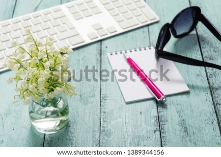 keypad, ring binder, pink pen, sunglasses and white flower bunch on blue table
