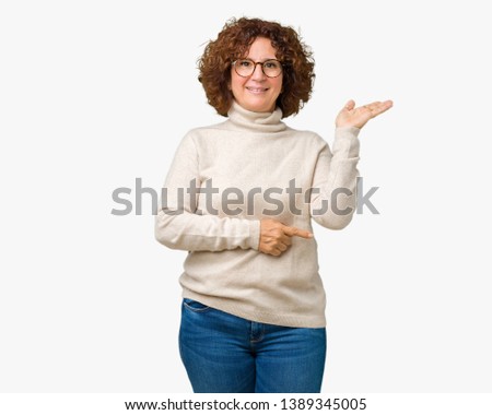 Beautiful middle ager senior woman wearing turtleneck sweater and glasses over isolated background smiling cheerful presenting and pointing with palm of hand looking at the camera.