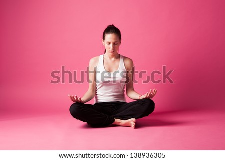 young woman in meditating yoga position studio shot pink background